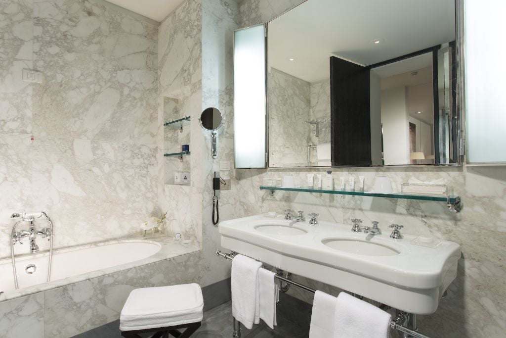 Luxurious Roma suite with elegant marble bathroom, plush king bed, ornate Italian furnishings, and panoramic view of Via Condotti's historic streetscape