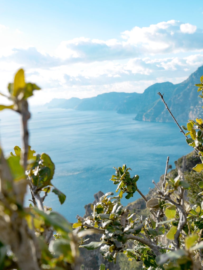 Pastel-colored houses nestled on steep cliffs overlooking turquoise Mediterranean waters, with luxury yachts dotting Amalfi's picturesque harbor