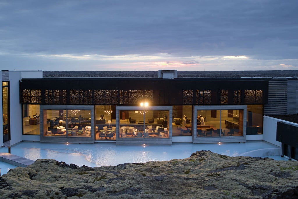 Luxurious minimalist Icelandic hotel suite with panoramic lagoon view, sleek white decor, floor-to-ceiling windows revealing dramatic volcanic landscape beyond