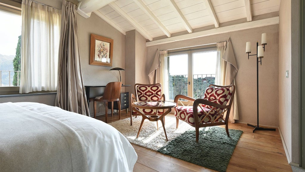 Elegant Tuscan-style hotel room with soft neutral tones, plush white linens, rustic wooden furniture, and large windows overlooking scenic countryside landscape