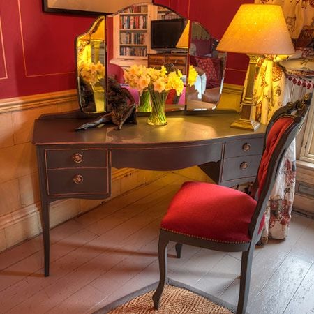 Elegant red-themed luxury suite with plush king bed, ornate gold-framed mirror, rich velvet curtains, and sophisticated period decor at historic boutique hotel