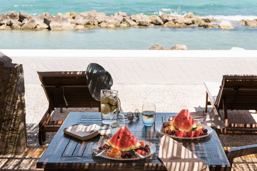 Luxurious Italian seaside hotel with elegant blue-tiled pool overlooking azure waters, nestled against dramatic coastal landscape of rocky cliffs and Mediterranean vegetation