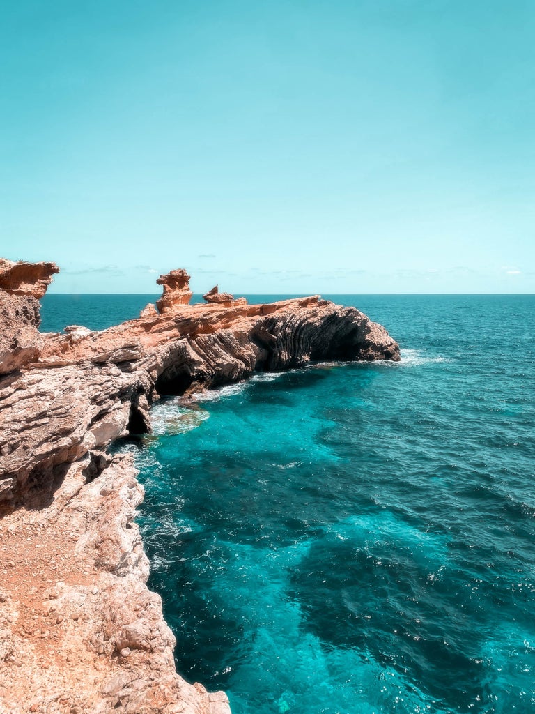 Sunset aerial view of Ibiza's picturesque coastline featuring luxury yachts in crystal-clear Mediterranean waters and whitewashed villas