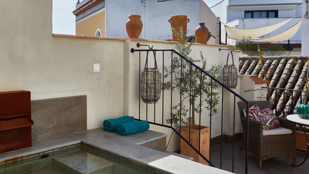 Elegant rooftop terrace with plunge pool, plush loungers and rustic stone walls overlooking Seville's historic skyline at sunset.