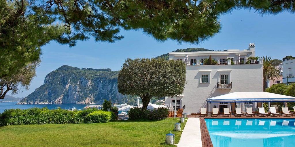 Elegant Italian hotel perched on Capri's cliffside, featuring white columns, Mediterranean architecture and panoramic sea views at dusk