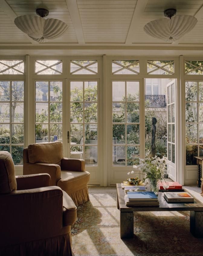 Elegant Parisian suite with plush velvet headboard, antique chandelier, soft neutral tones, and expansive window overlooking urban French streetscape