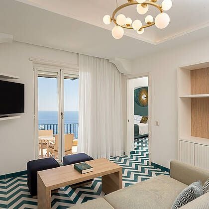 Elegant marble-clad Hotel Luna suite in Italian style, featuring plush king bed, panoramic windows overlooking scenic coastline, and refined contemporary decor