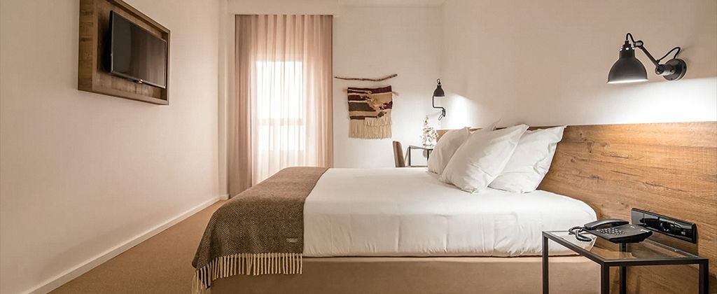 Elegant Portuguese hotel room with soft neutral tones, plush bedding, and expansive garden view through large windows at Lamego Hotel & Life