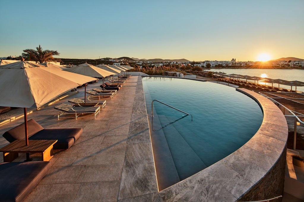 Pristine infinity pool overlooking Aegean Sea at sunset, with white cubist architecture and luxurious daybeds framing the coastal view