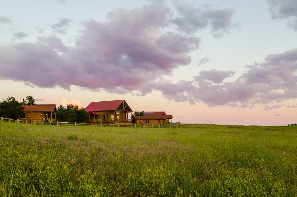 Rustic luxury lodge nestled in scenic mountain landscape, with wooden cabins, lush greenery, and dramatic sunset illuminating the tranquil Scenset Mountain Ranch setting