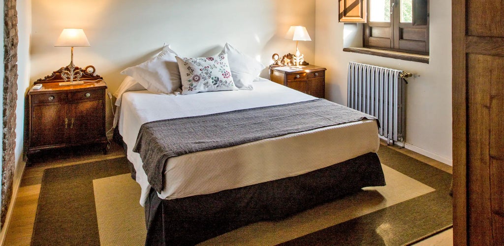 Elegant Spanish luxury suite with white-washed walls, rustic wooden furniture, and soft natural light streaming through arched windows at Cortijo del Marqués