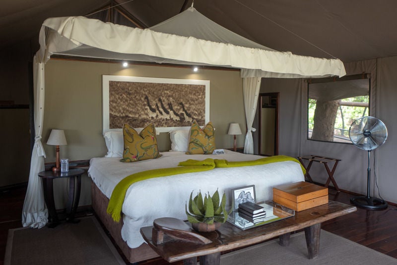 Luxurious safari lodge nestled in Botswana wilderness, featuring elevated wooden walkways connecting thatched-roof suites overlooking savanna