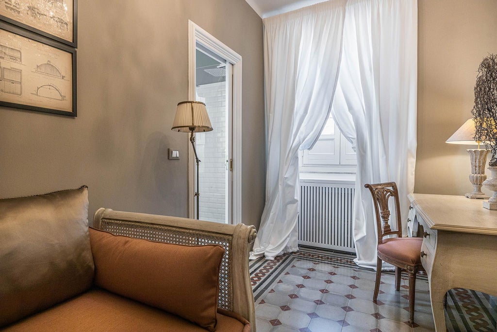 Elegant deluxe studio with soft neutral tones, plush white bedding, modern minimalist furniture, and large windows overlooking Italian architectural landscape