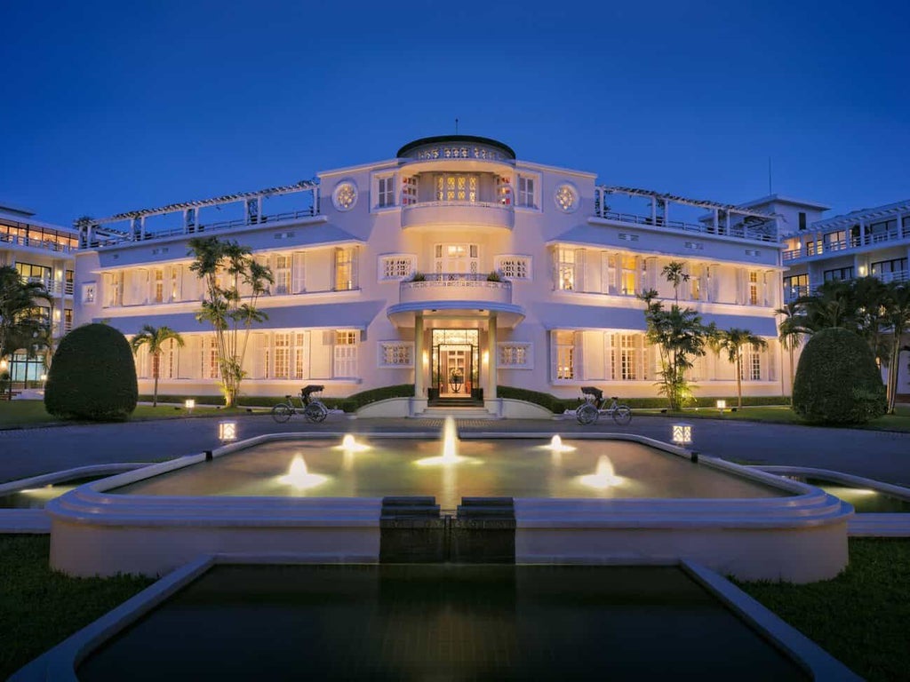 Elegant French colonial-style hotel with white facade, lush tropical gardens, and traditional architecture overlooking serene Perfume River in Hue, Vietnam