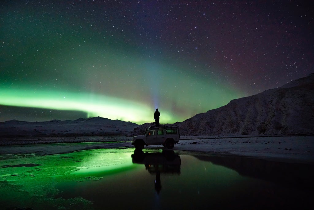 Vibrant green and purple aurora borealis dancing across a starry night sky over a snow-covered Icelandic landscape with distant mountain silhouettes