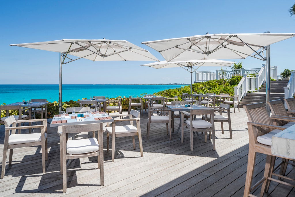 Elegant beachfront resort with white Mediterranean-style buildings nestled among palm trees, facing turquoise waters and pristine beach