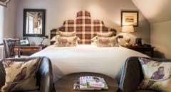 Classic room in historic Lygon Arms hotel, featuring elegant traditional decor with plush bedding, antique furniture, and soft neutral color palette reflecting British countryside charm.