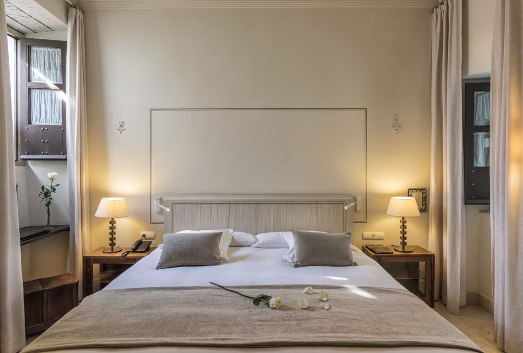 Elegant historic Spanish hotel room with ornate wooden ceiling, antique furnishings, and large windows overlooking traditional Córdoba architecture at golden hour