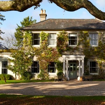 Luxurious country hotel nestled in lush Devon countryside, featuring stone facade, rolling green hills, and elegant outdoor terrace with rustic charm