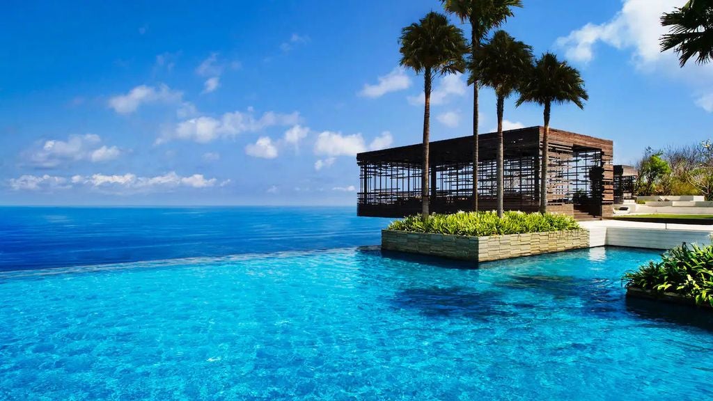 Luxurious infinity pool overlooking Bali's dramatic cliffs at sunset, with modern pavilions and ocean views stretching to the horizon