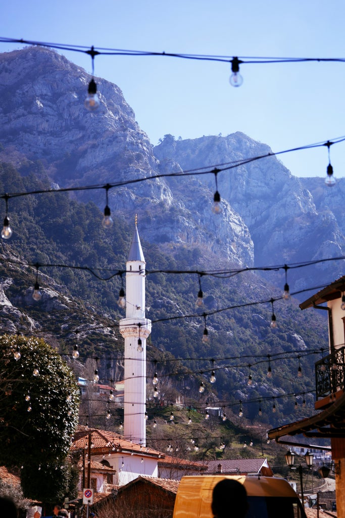 Scenic panorama of Kruja Castle against rugged Dajti Mountains, showcasing Albanian landscape with stone walls, lush greenery, and distant mountain peaks