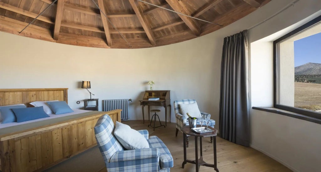 Elegant stone suite at Cortijo del Marqués with rustic wooden beams, plush white bedding, and panoramic views of Spanish countryside landscape