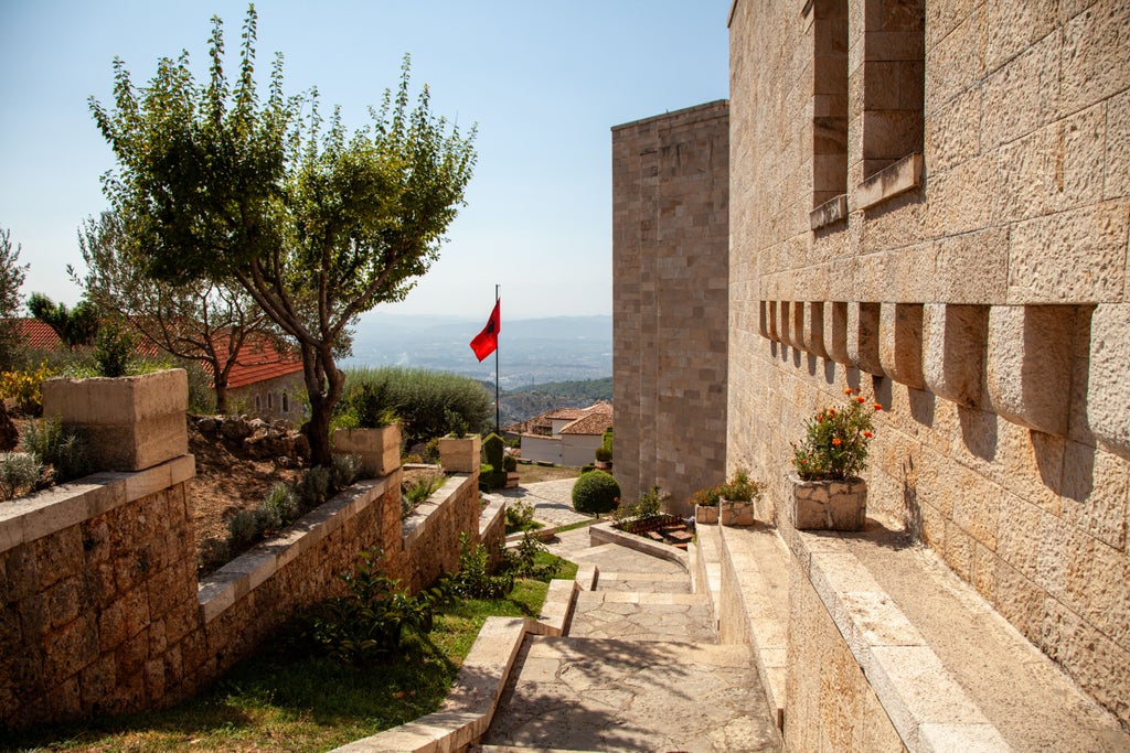 Panoramic view of Kruja Castle nestled against rugged Dajti Mountains, showcasing Albanian landscape with historic stone walls and lush green terrain