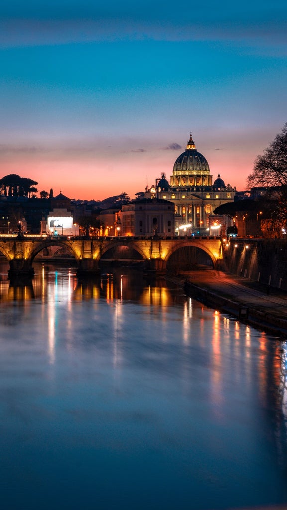 Majestic Colosseum illuminated at dusk, with ancient Roman Forum ruins and Mediterranean cypress trees against pink-orange sky