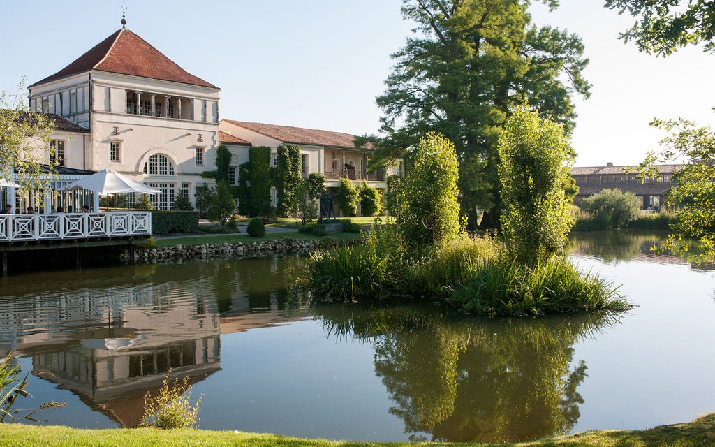 Alt: Elegant French wine country hotel with stone & timber facade nestled among vineyard rows, featuring rustic-luxe architecture and warm lighting