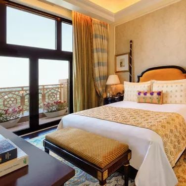 Opulent hotel suite with elegant gold and cream decor, expansive king bed, ornate chandelier, and panoramic city views of New Delhi's skyline