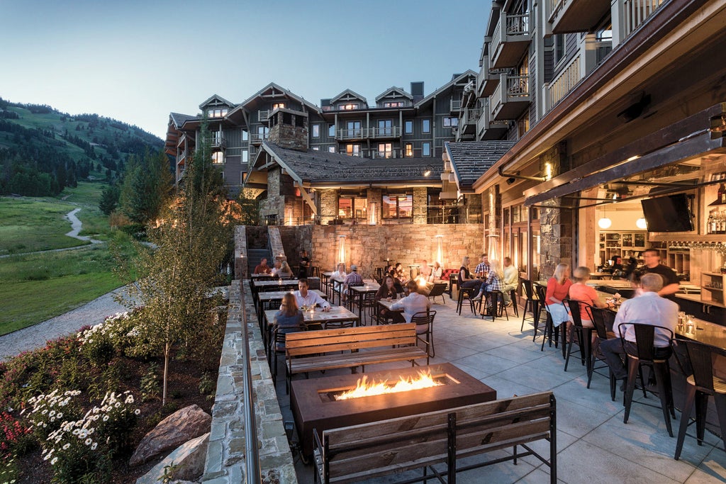 Snow-capped mountains frame luxury stone and timber lodge with panoramic windows, grand fireplaces, and scenic outdoor terrace seating