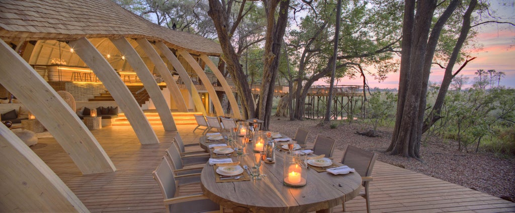 Luxurious eco-lodge with curved wooden architecture nestled among palm trees overlooking Okavango Delta's pristine waterways at sunset