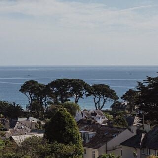 Elegant coastal hotel with white facade, large windows, and manicured gardens, nestled against a serene beach backdrop in a picturesque United Kingdom seaside setting