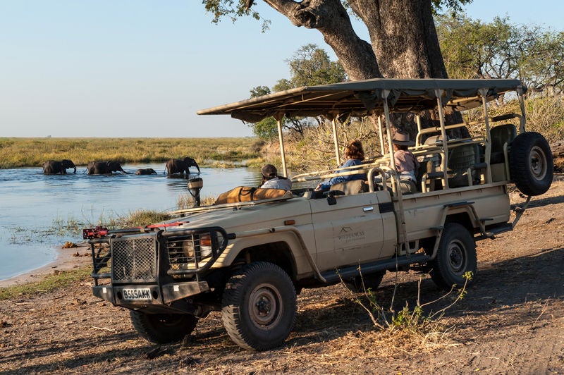 Elevated wooden safari tent overlooking African savanna at sunset, with private deck, canvas walls and thatched roof design