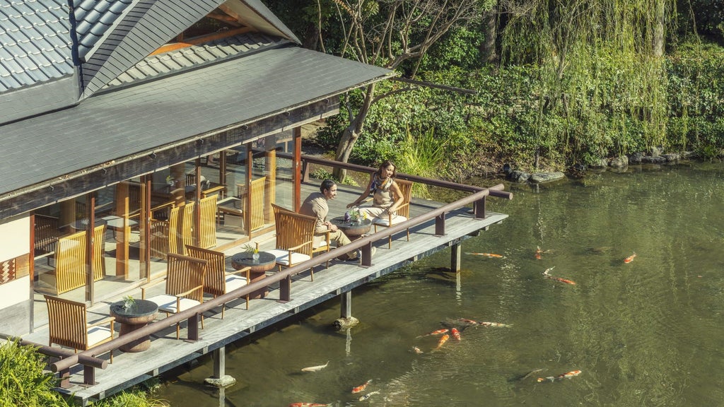 Traditional Japanese garden at Four Seasons Kyoto featuring serene pond, arched stone bridge, manicured trees and tranquil bamboo grove