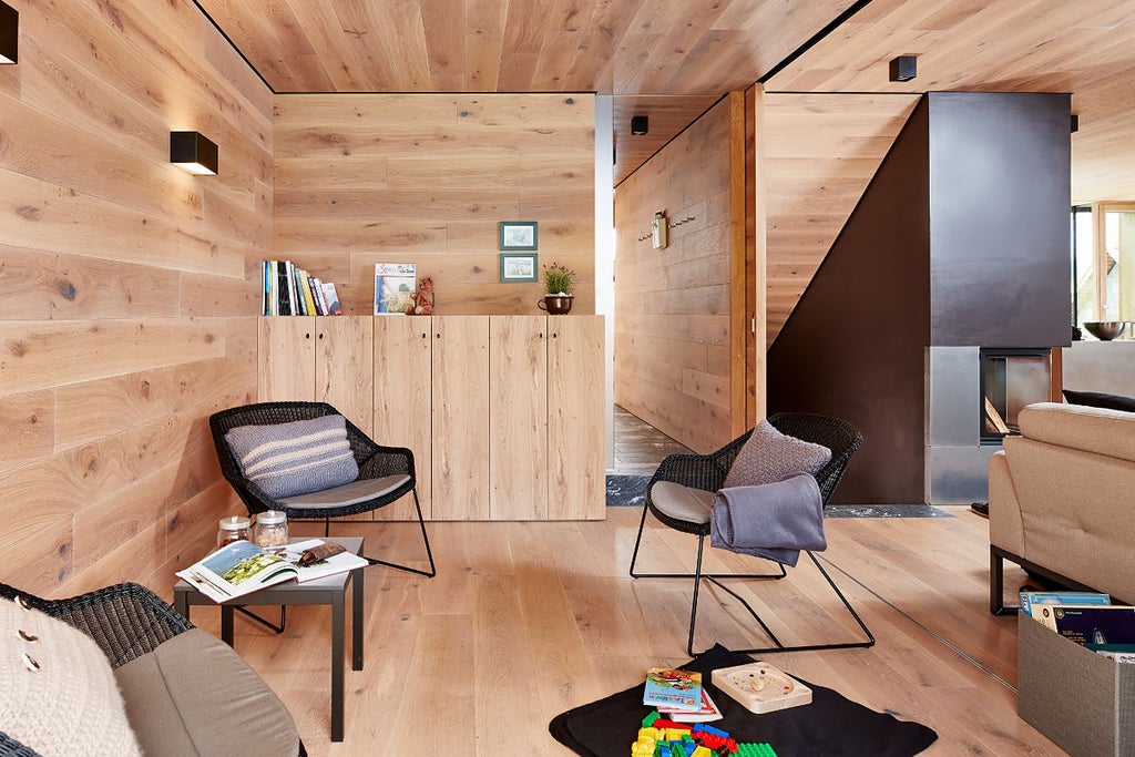 Modern wooden and glass hotel nestled in Austrian mountainside, featuring panoramic balconies and surrounded by snow-capped Alpine peaks