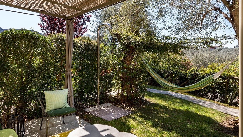 Elegant Tuscan garden with lush greenery, rustic stone walls, and sunlit terrace of Locanda al Colle boutique hotel near Camaiore, overlooking rolling countryside