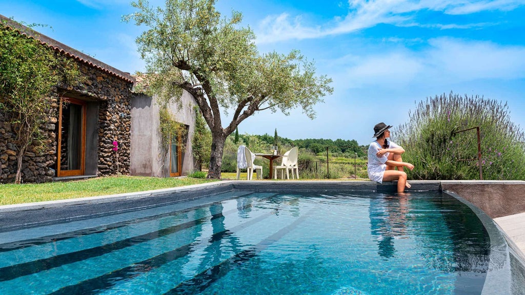 Elegant pool suite at Monaci delle Terre Nere, nestled in Sicilian landscape with lush greenery, minimalist design, and infinity pool overlooking volcanic terrain