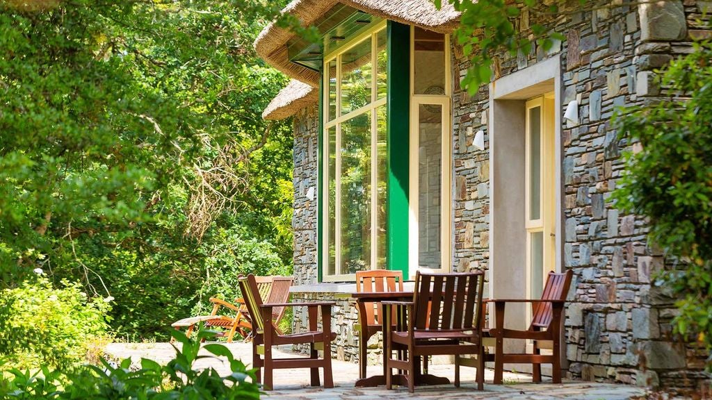 Luxurious Garden Cottage living room with stone fireplace, plush furniture, hardwood floors and scenic riverside windows at Sheen Falls Lodge