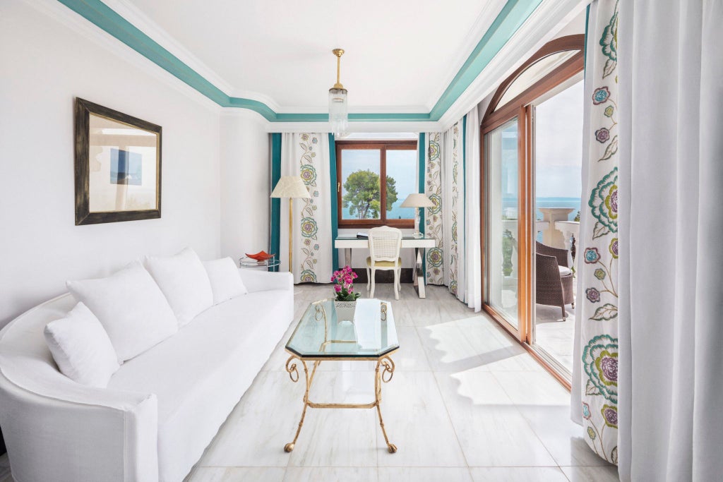 Elegant Deluxe Junior Suite with panoramic Aegean Sea view, plush white bed, wooden floors, and private balcony at luxurious Greece resort