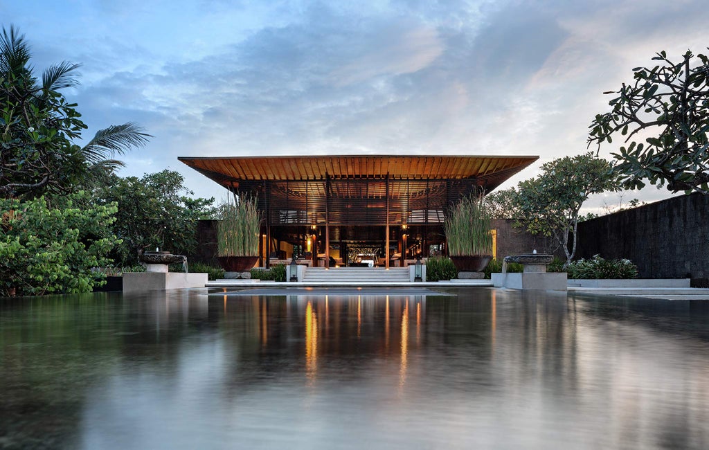 Modern beachfront villa with infinity pool overlooking ocean at sunset, featuring sleek architecture and tropical landscaping in Bali