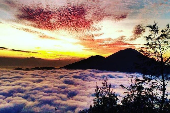 Sunrise hike on Mount Batur, Bali: Misty volcanic landscape with silhouetted trekkers against golden morning light and lush Indonesian terrain