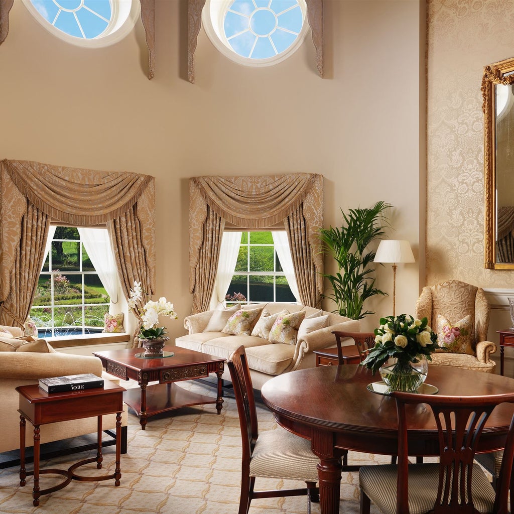 Opulent royal suite with plush king bed, elegant cream and gold color palette, panoramic windows overlooking manicured hotel grounds in luxurious UK estate setting