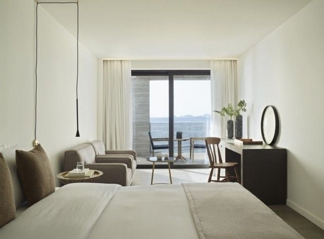 Luxurious white-themed suite with panoramic Aegean Sea view, minimalist design, king-sized bed, and elegant contemporary Greek island decor