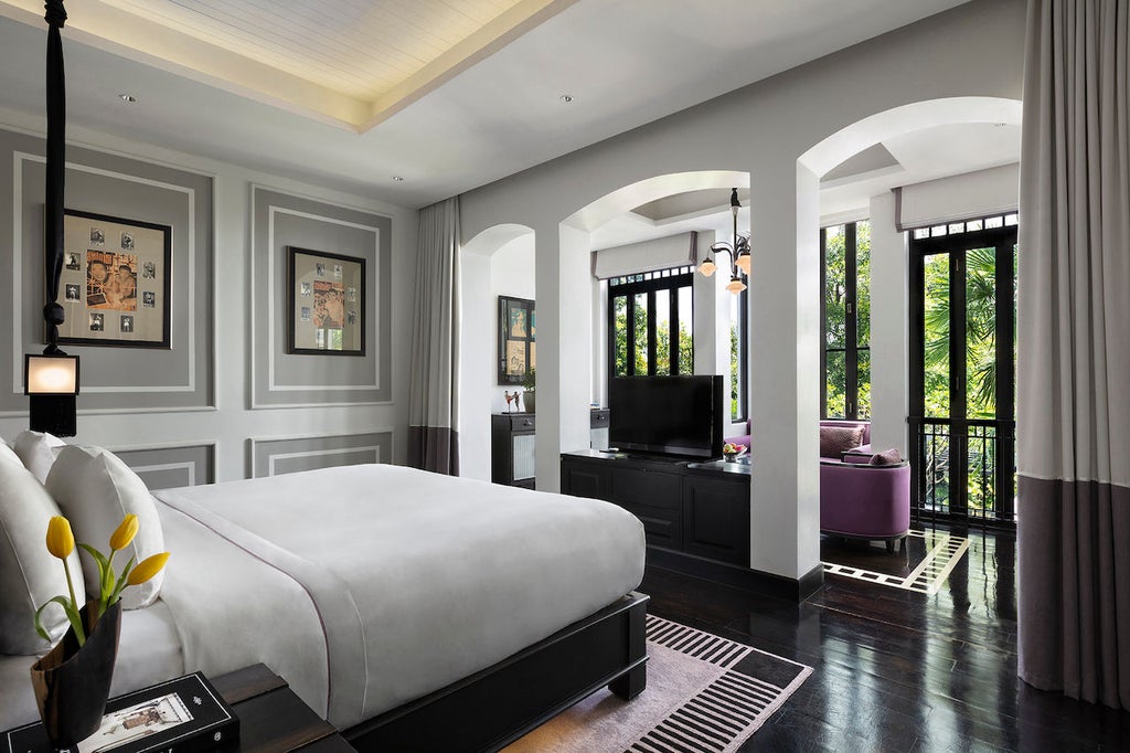 Luxurious garden suite with floor-to-ceiling windows, elegant dark wood furnishings, plush king bed, and traditional Thai decor accents