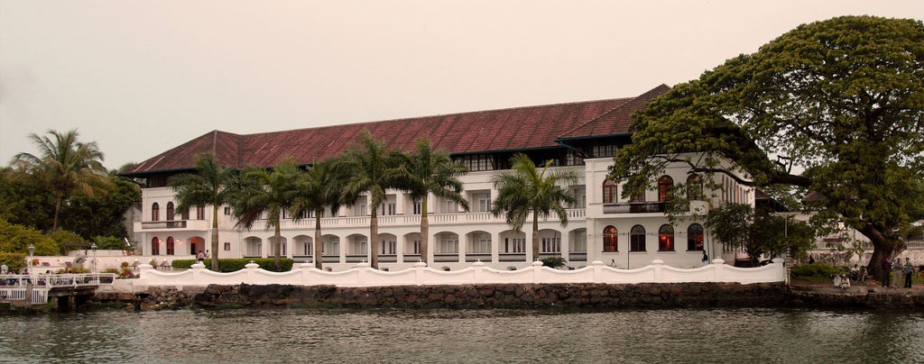 Colonial-style luxury hotel facade featuring whitewashed walls, ornate columns, and waterfront location overlooking Chinese fishing nets in Kerala