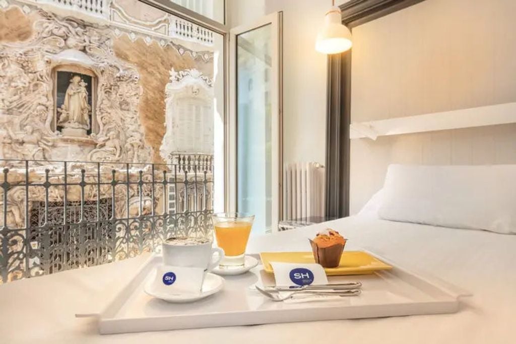 Elegant luxury boutique hotel facade in Valencia with ornate baroque architecture, classic stone balconies and arched windows at dusk