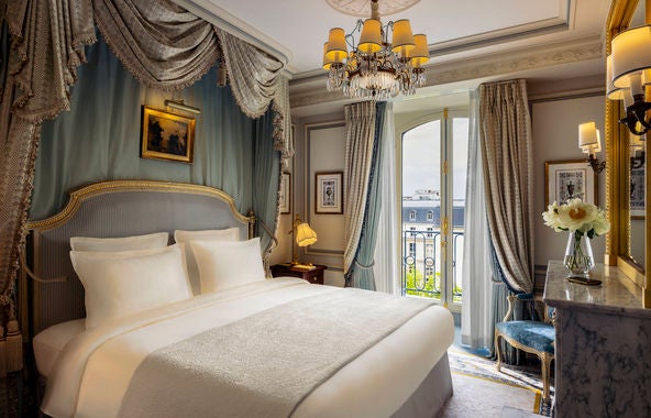 Elegant Parisian suite with crystal chandelier, gold-framed mirrors, plush period furniture, and tall windows with silk drapes