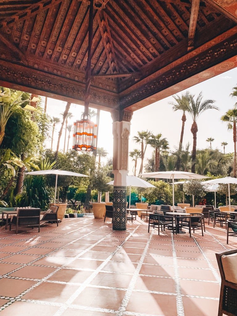 Grand Moroccan palace hotel with ornate archways, intricate tilework, and manicured gardens reflecting in a serene turquoise pool at dusk