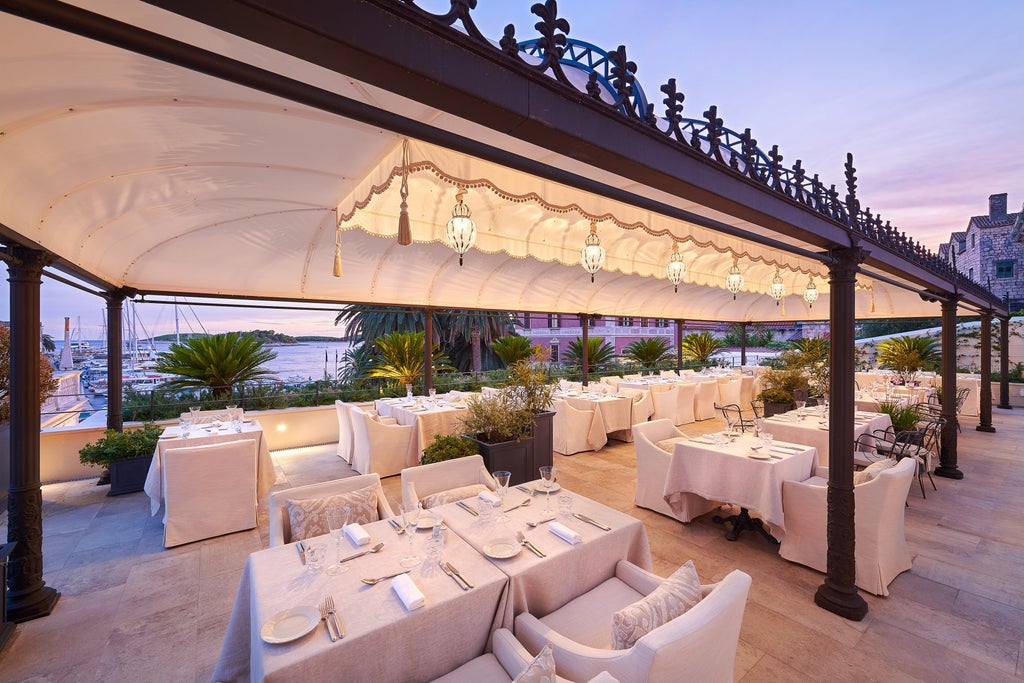 Elegant stone facade of Hotel Palace Elizabeth with ornate balconies and arched windows overlooking Hvar's historic marina at sunset